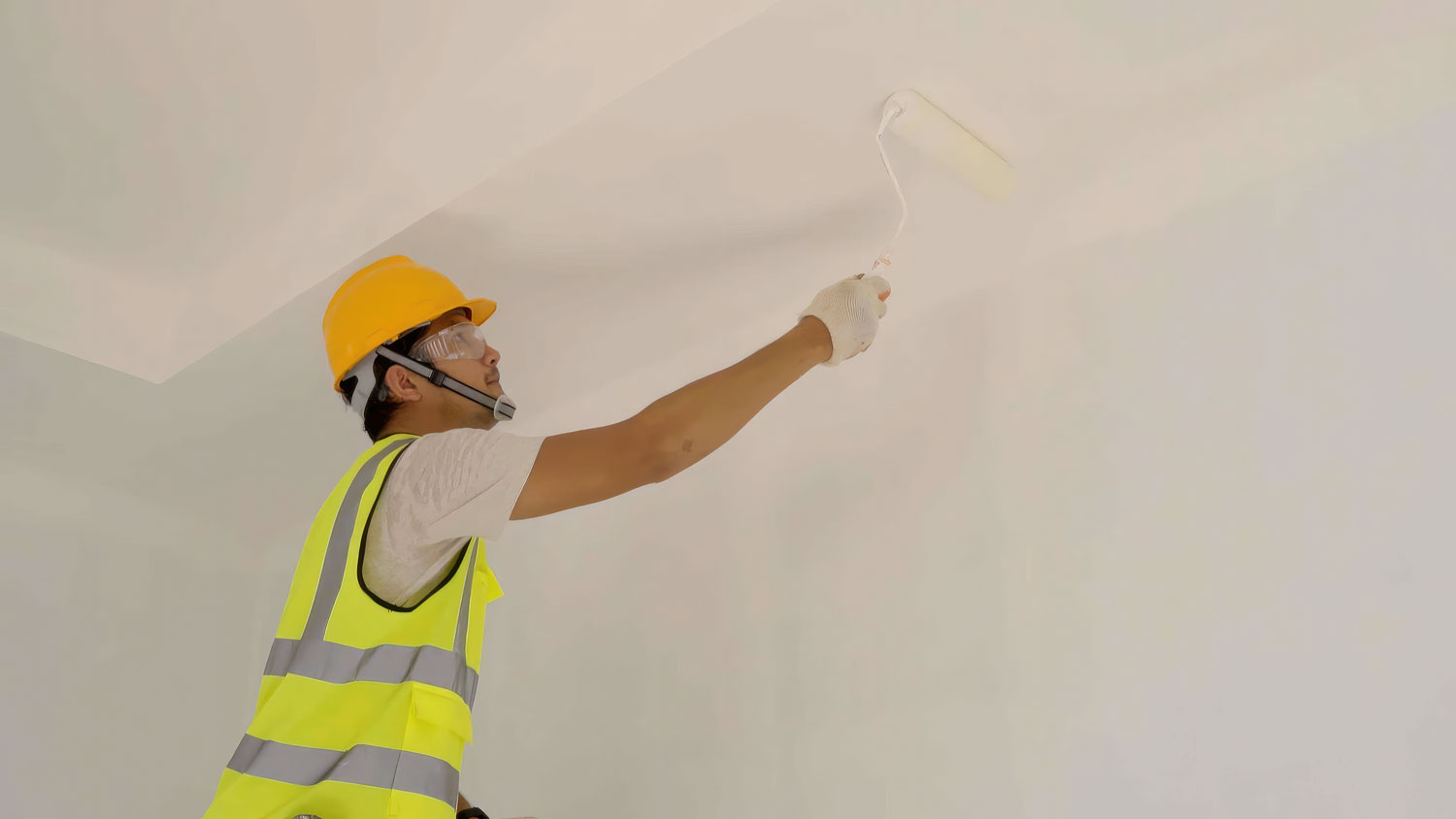 Person performing interior painting inside home using roller on wall
